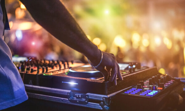 Dj mixing outdoor at beach party festival with crowd of people i Dj mixing outdoor at beach party festival with crowd of people in background - Summer nightlife view of disco club outside - Soft focus on hand - Fun ,youth,entertainment and fest concept